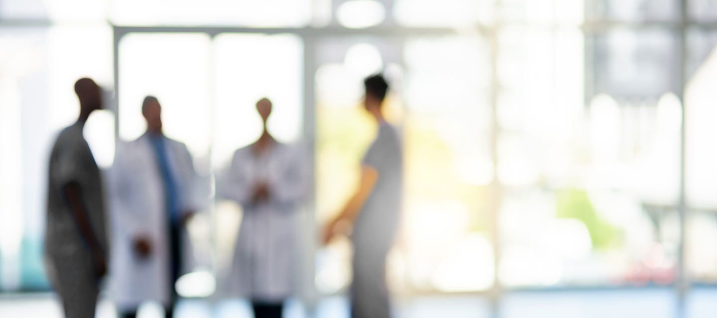 Four physicians talking in sunny hospital lobby