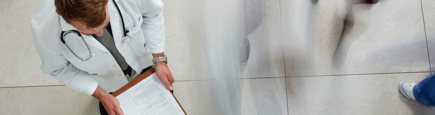 Male doctor looking at a patient's file in a busy hospital from above.