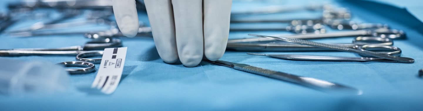 Closeup of surgeon's hand picking up surgical tools from tray.