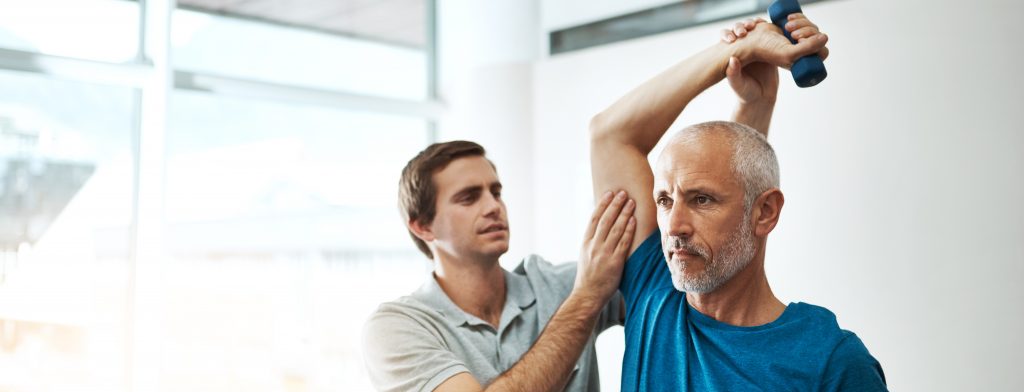 Young male physical therapist helping a client with stretching exercises in his office during the day.