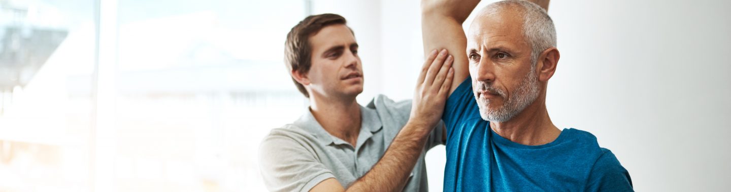 Young male physical therapist helping a client with stretching exercises in his office during the day.